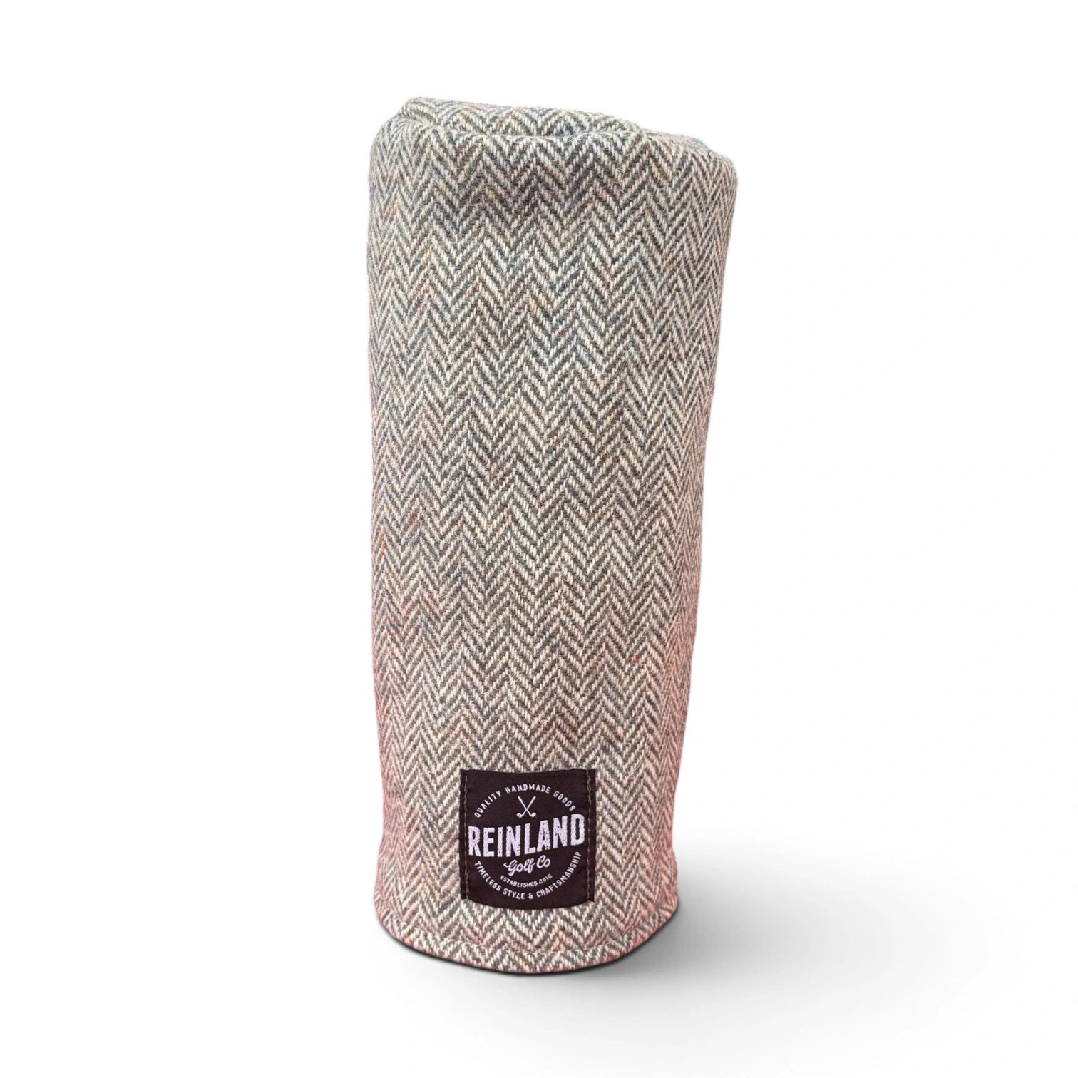 A golf club headcover made of a beige and gray herringbone tweed fabric, featuring a black square patch with the Reinland Golf Club logo near the bottom.