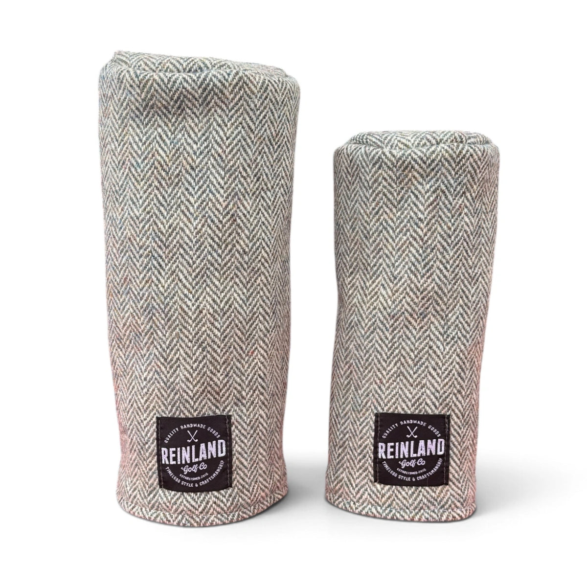 Two golf club headcover sleeves in a gray and beige herringbone tweed fabric, standing upright on a white background. Each sleeve features a black square patch at the bottom with the 'Reinland Golf Co' logo.