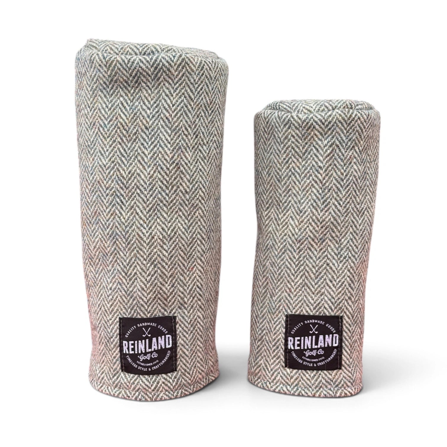 Two golf club headcover sleeves in a gray and beige herringbone tweed fabric, standing upright on a white background. Each sleeve features a black square patch at the bottom with the 'Reinland Golf Co' logo.