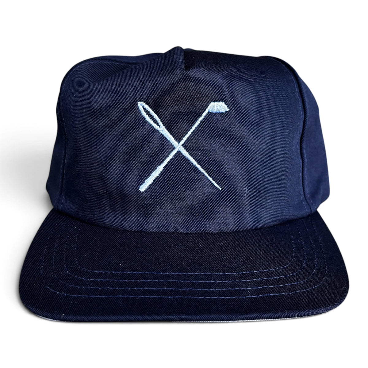 A navy blue snapback cap featuring an embroidered white crossed golf club graphic on the front panel, set against a plain white background.