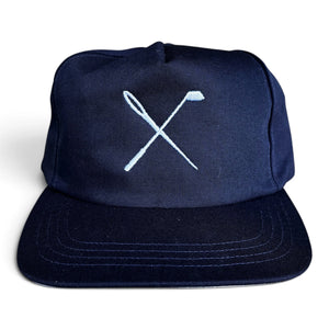 A navy blue snapback cap featuring an embroidered white crossed golf club graphic on the front panel, set against a plain white background.